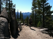 kid on mountain bike next to big boulder with mountains in distance