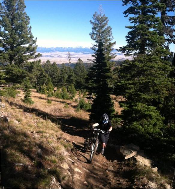 kid pushing bike on trail with snowy mountains in distance